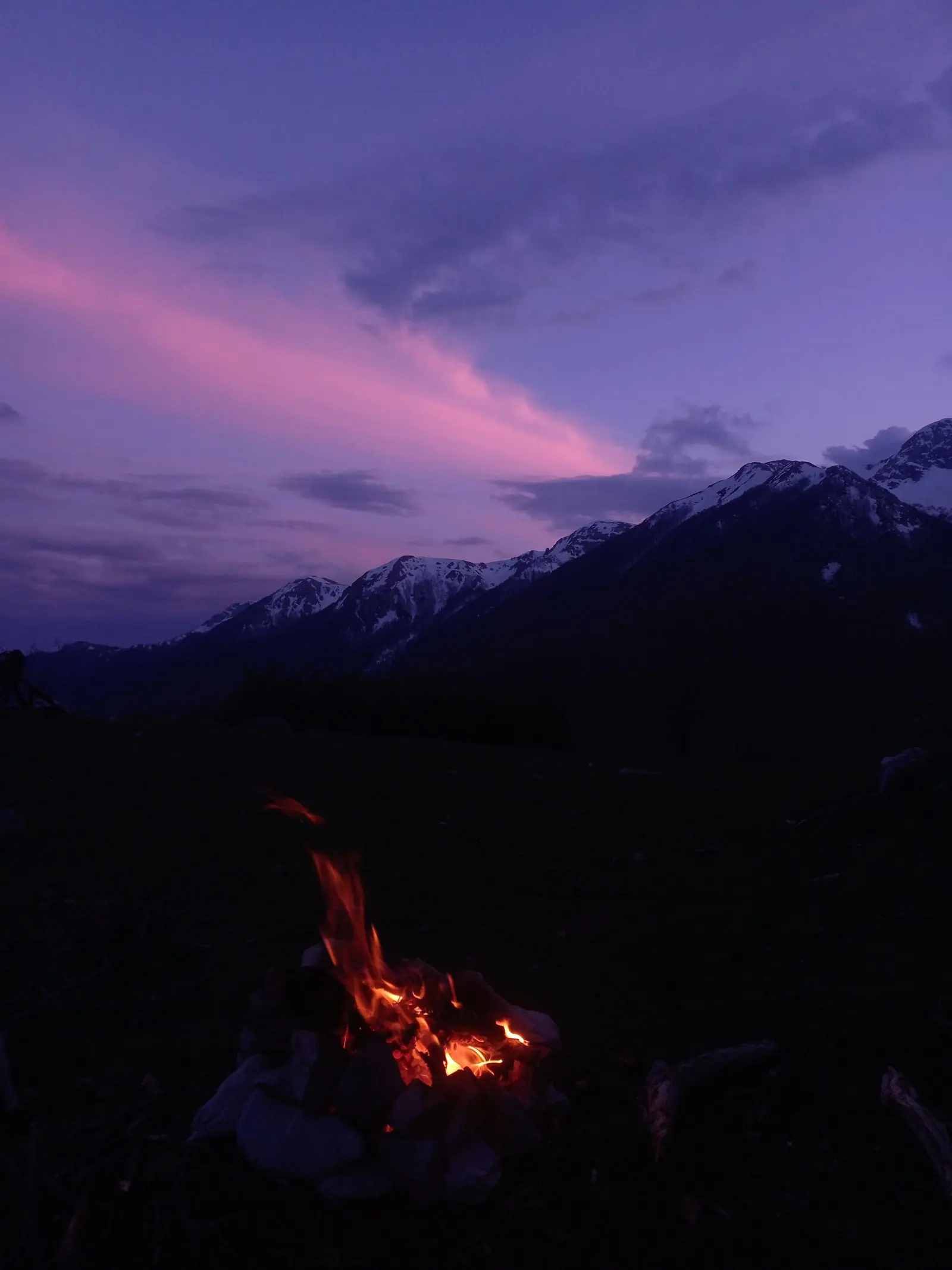 A campfire at dusk beneath the mountains (illustrative photo)